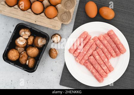 Saucisses de petit déjeuner au poulet, champignons Beby Bella, œufs, gros plan, plat.Ingrédients crus sur la table de cuisine Banque D'Images