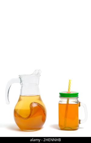 Boisson rafraîchissante d'été faite de kombucha dans un pot et une tasse avec paille sur fond blanc Banque D'Images