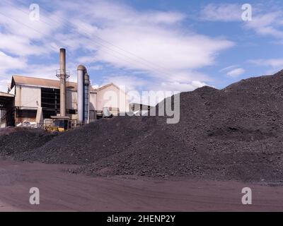 Tas de charbon utilisé pour produire de la vapeur avec des chaudières dans une usine industrielle.Cheminée de la chaudière en arrière-plan. Banque D'Images