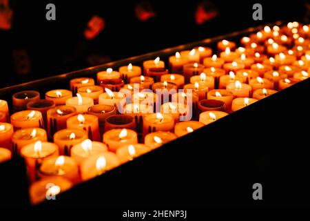 Les bougies votives brûlent sur un stand dans une église dans l'obscurité Banque D'Images