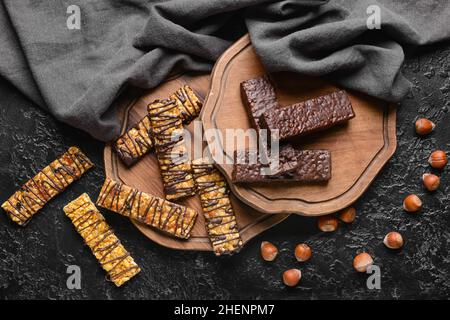 Planches avec de savoureuses barres de noix de chocolat sur fond sombre Banque D'Images