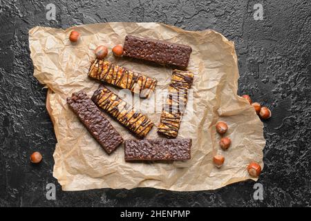 Parchemin avec de savoureuses barres de noix de chocolat sur fond sombre Banque D'Images