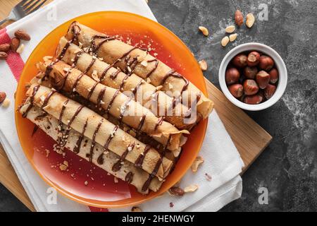 Assiette de crêpes fines savoureuses avec pâte de chocolat et noix sur fond noir Banque D'Images