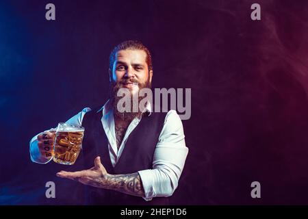 Un homme à barbe heureux tient une savoureuse bière pression à la main tout en faisant des gestes.Boisson, concept de la fête d'octobre. Banque D'Images