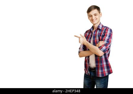 Un jeune homme souriant vêt de vêtements décontractés a traversé les bras sur sa poitrine et pointe son doigt sur un fond vide avec de l'espace pour le texte.Promotions, disque Banque D'Images