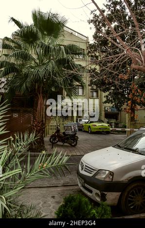 Isfahan, NOR Julfa, Iran, 16, novembre,2021: Section d'une rue dans NOR Julfa avec parking pour voitures, scooters, sous les arbres et palmiers sur un caillou Banque D'Images