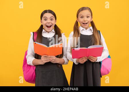 Surpris les enfants dans les uniformes formels lire les livres scolaires fond jaune, bibliothèque Banque D'Images