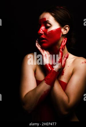 Creative portrait d'une jeune fille. Le visage est peint avec des paillettes rouges de la peinture. Le triangle est dessiné sur le visage. Profil de modèle sur fond noir Banque D'Images