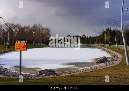 Lac artificiel partiellement gelé et fontaine à un parc de la ville et orange pas de signe de natation Banque D'Images