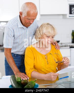 Couple d'âge mûr à la table de cuisine remplissant les documents Banque D'Images