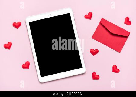 Tablette numérique pour choisir des cadeaux, faire l'achat, enveloppe, coeur rouge sur table rose vue du dessus plat Lay liste d'achats de vacances, bonne Saint-Valentin Banque D'Images