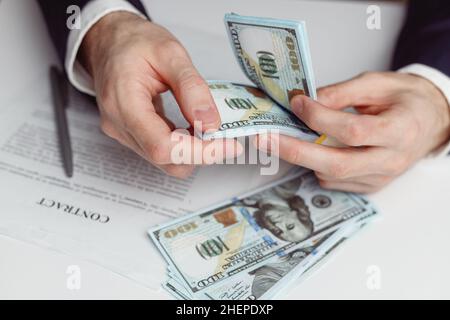 L'homme en costume compte de l'argent avant de signer le contrat.Gros plan des mains avec de l'argent US dollars Banque D'Images