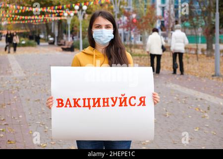 Une femme dans un masque médical tient une affiche avec une inscription, traduite de l'ukrainien se faire vacciner Banque D'Images