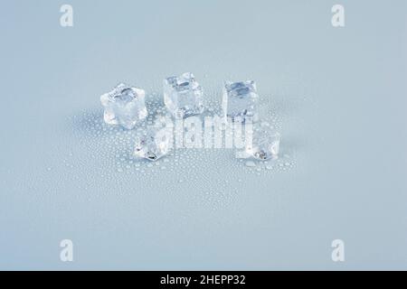 Cubes de glace dispersés sur une table sur fond gris en gouttes d'eau de fonte Banque D'Images