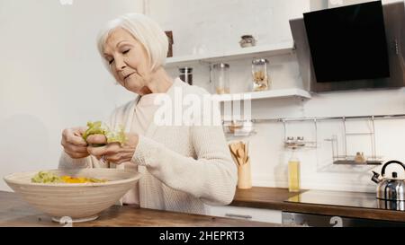 femme âgée ajoutant de la laitue fraîche au poivron en tranches tout en préparant la salade pour le dîner d'action de grâce Banque D'Images