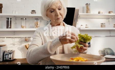 femme âgée préparant une salade de légumes et ajoutant de la laitue fraîche dans un bol Banque D'Images