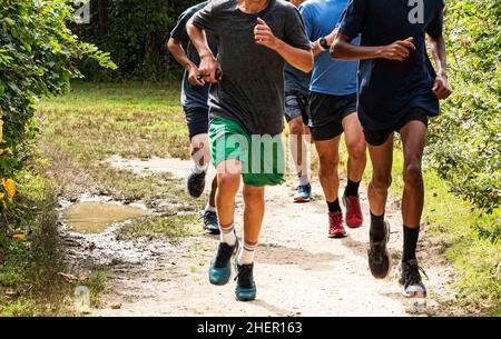 Vue de face des garçons du lycée qui s'exécutent ensemble sur un chemin de terre dans un parc d'entraînement pour leur équipe de cross-country. Banque D'Images