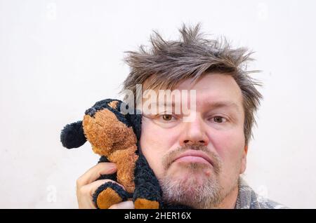 Portrait d'un homme qui se vriller avec un jouet pour chien.Un homme avec des cheveux rouillés et emmêlés appuie sa joue contre le jouet bourré.Intérieur.Mise au point sélective. Banque D'Images