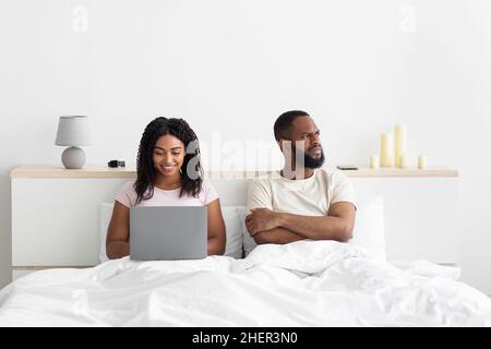 Offensé, le jeune africain américain triste avec les bras croisés sur sa poitrine ignore la femme avec l'ordinateur Banque D'Images