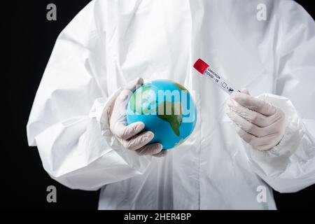 vue rognée d'un scientifique en costume blanc noisette tenant le globe et le test de variante covid-19 omicron isolé sur image noire Banque D'Images