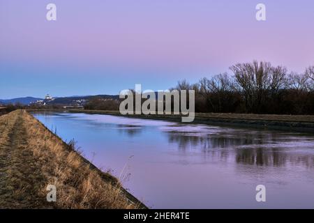 Paysage en début de soirée avec voie navigable au coucher du soleil.Magnifique ciel coloré, reflet sur la surface de l'eau.Château en arrière-plan.Trencin, Slovaquie. Banque D'Images