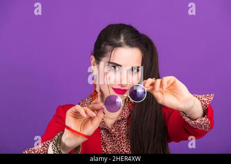 Jeune belle femme dans le style 90s montre des lunettes rondes à l'appareil photo. Banque D'Images