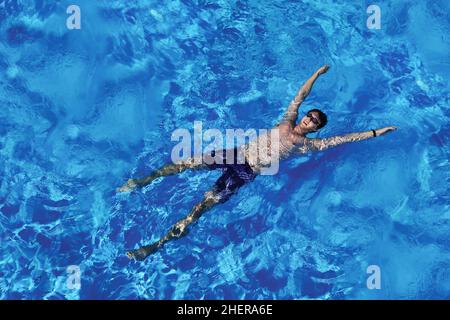 Jeune homme caucasien flottant sur de l'eau bleue dans la piscine.Vue de dessus.Vacances d'été, détente, tourisme en vacances Banque D'Images