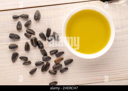 Beaucoup de délicieuses graines de tournesol avec une soucoupe d'huile de tournesol sur une table en bois, vue rapprochée, vue de dessus. Banque D'Images