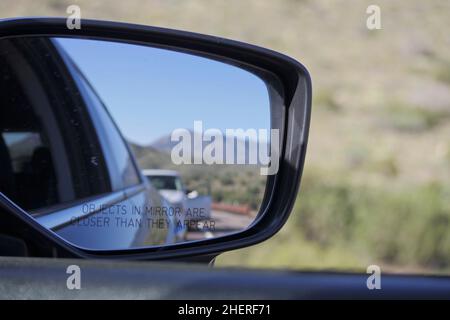 En regardant la circulation, sur une route montagneuse du nord de l'Arizona, à travers le miroir de vue latérale avec des voitures et des montagnes en arrière-plan. Banque D'Images