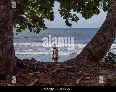 Deux hommes marchant sur une plage des Caraïbes à Playa Cahuita, Costa Rica encadré par deux grands arbres. Banque D'Images