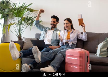 Un heureux couple réservant un hôtel en ligne avec un ordinateur portable et une carte de crédit, assis avec des valises, des passeports et des billets Banque D'Images