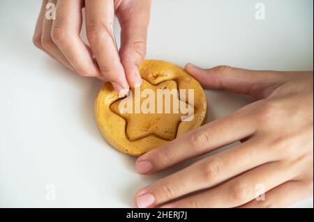 Les mains de gros plan scratch cassent sucre caramel bonbons biscuits avec une aiguille en métal en forme d'étoile sur un fond blanc. Banque D'Images