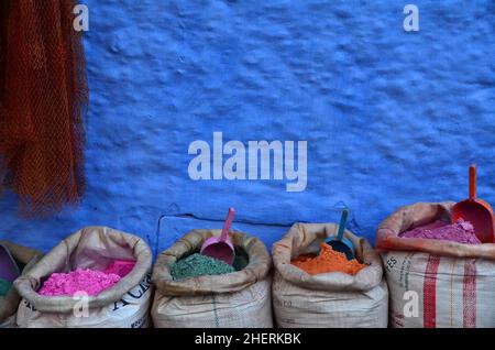 Poudre de peinture colorée en sacs devant le mur bleu avec pelle, Chefchaouen, Maroc Banque D'Images