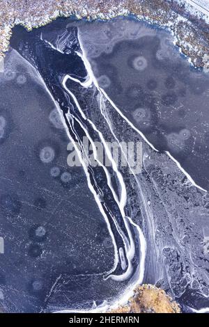 Vue aérienne sur un étang gelé recouvert de glace avec d'énormes fissures et motifs Banque D'Images