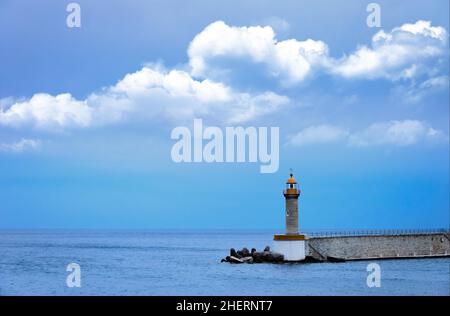 Un phare sur la rive d'un quai, un phare entouré de rochers à ciel bleu Banque D'Images