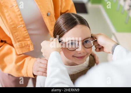 ophtalmologiste flou mettant des lunettes sur la fille positive dans le magasin optique Banque D'Images