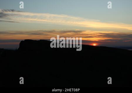 Coucher de soleil sur Arthur's Seat (Édimbourg, Écosse, Royaume-Uni). Un soleil rouge et orange éclatant s'enfonçant sous l'horizon avec la silhouette d'Arthur's Seat à l'avant Banque D'Images