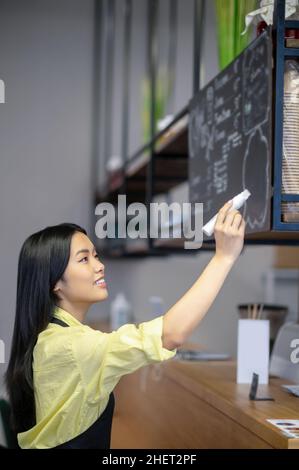 Une jeune femme asiatique écrit un menu à bord dans un café Banque D'Images