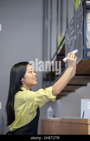 Une jeune femme asiatique écrit un menu à bord dans un café Banque D'Images