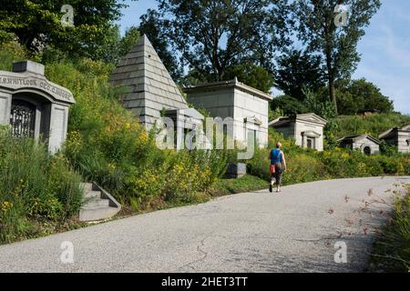 Brooklyn, New York, États-Unis - 23 juillet 2020 : une femme marchant sur un sentier bordé de mausolées et de prairies de fleurs sauvages, cimetière de Greenwood Banque D'Images