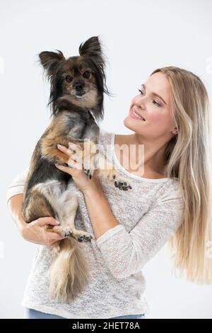 Une femme blonde aux cheveux longs tient un petit chien dans ses bras et le regarde.Chien de race multiple. Banque D'Images