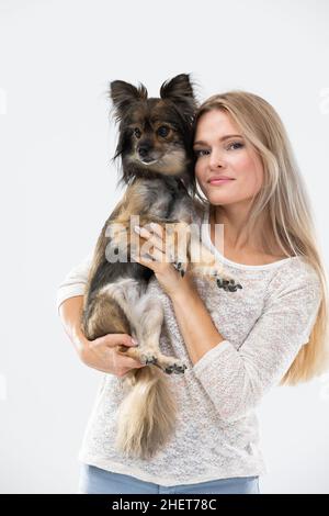 Une femme blonde aux cheveux longs tient un petit chien dans ses bras et le regarde.Chien de race multiple. Banque D'Images