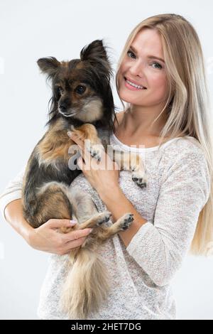 Elle tient un petit chien dans ses bras et sourit.Portrait d'une femme avec un chien.Chien de race multiple. Banque D'Images