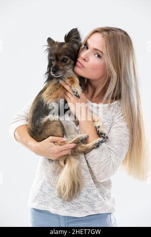 Une femme blonde aux cheveux longs tient un petit chien dans ses bras et le regarde.Chien de race multiple. Banque D'Images