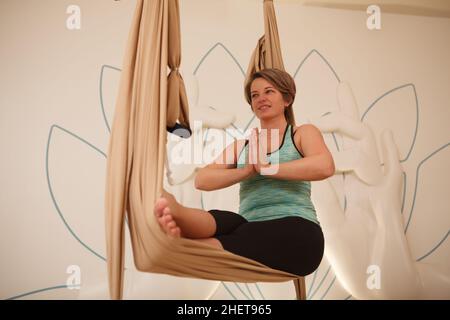 Photo d'une femme d'âge moyen qui se balance dans un hamac de yoga aérien Banque D'Images