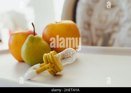 Grignoteuse avec pommes fraîches et poire sur table pour enfants, gros plan.Alimentation bébé. Banque D'Images