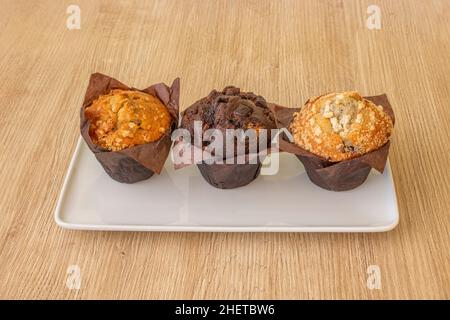 Un muffin au chocolat et deux autres sur une assiette blanche et une table en bois Banque D'Images