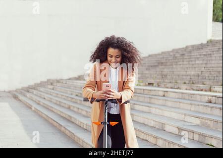 Une jeune femme télécharge l'application pour utiliser le scooter électrique en ville rue saine style de vie durable style de vie Banque D'Images