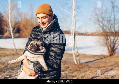 Jeune homme marchant chien de petit dans le parc d'hiver enneigé.Maîtrisez le jeu avec un animal qui le tient sur les mains à l'extérieur.Activités avec les animaux Banque D'Images