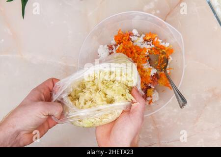 Un homme ajoute le chou congelé à la viande hachée pour les petits pains de chou paresseux sur la table. Banque D'Images